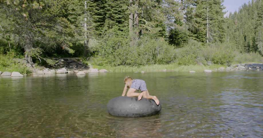 A boy is riding an inner tube on a lake on a natural day