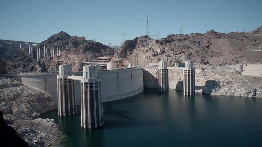 A huge dam sits between mountains as cars drive over the top of it