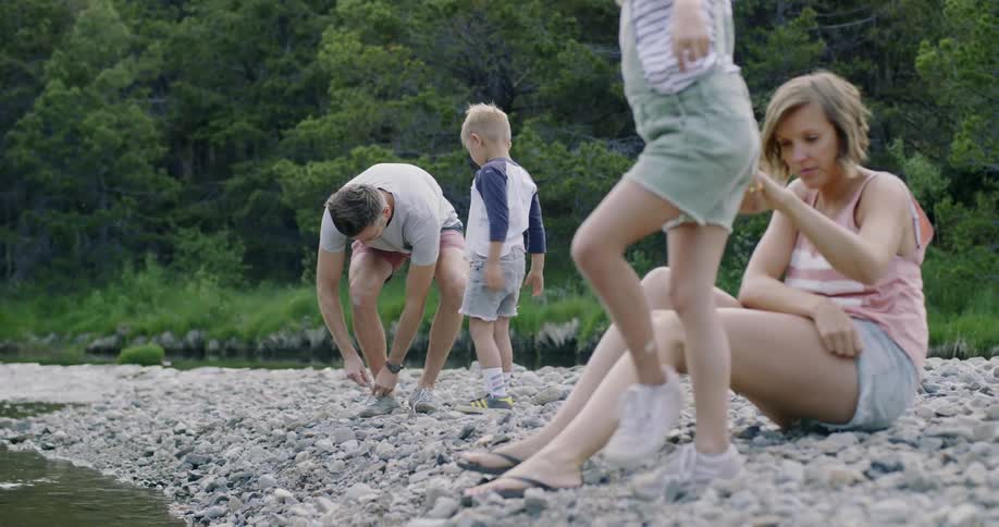 Family sits on a rocky shore next to a stream