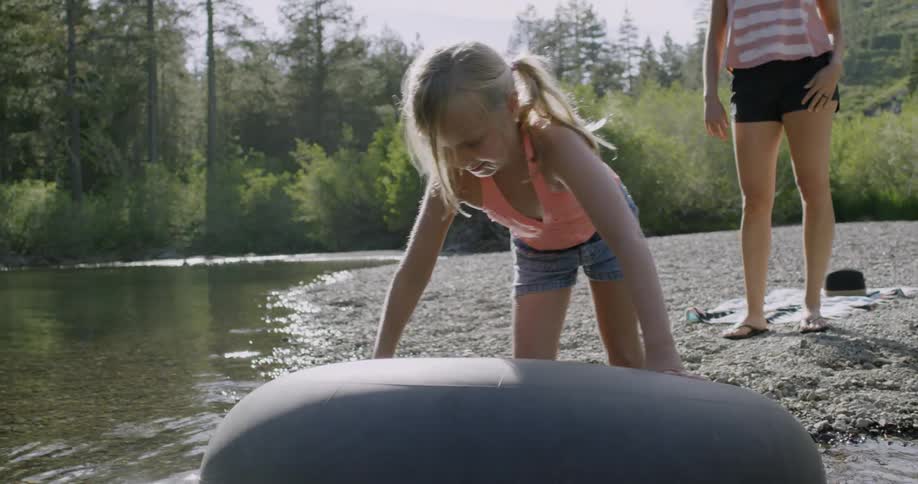Little girl wades out into river on inner tube