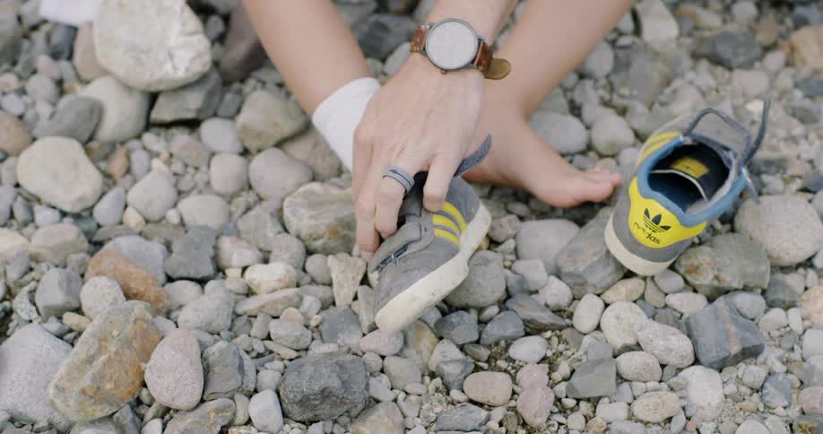 A man takes shoes off a boy while sitting on rocks