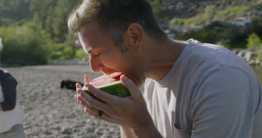 A man laughs while eating watermelon outside