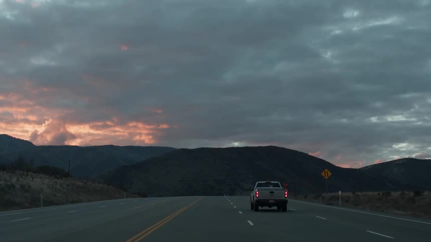 Cars traveling on mountain highway at cloudy sunset