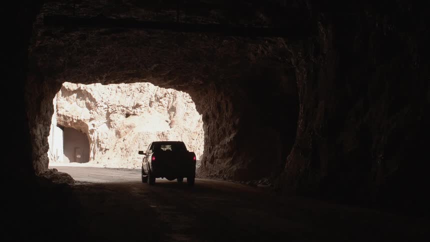 A pickup truck is driving through a tunnel in a desert landscape during the day