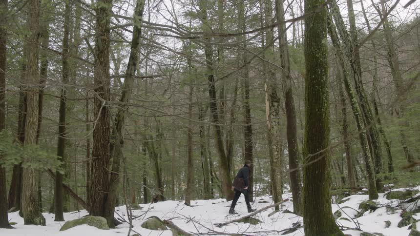 A man carrying a bag walks through the snow in the woods