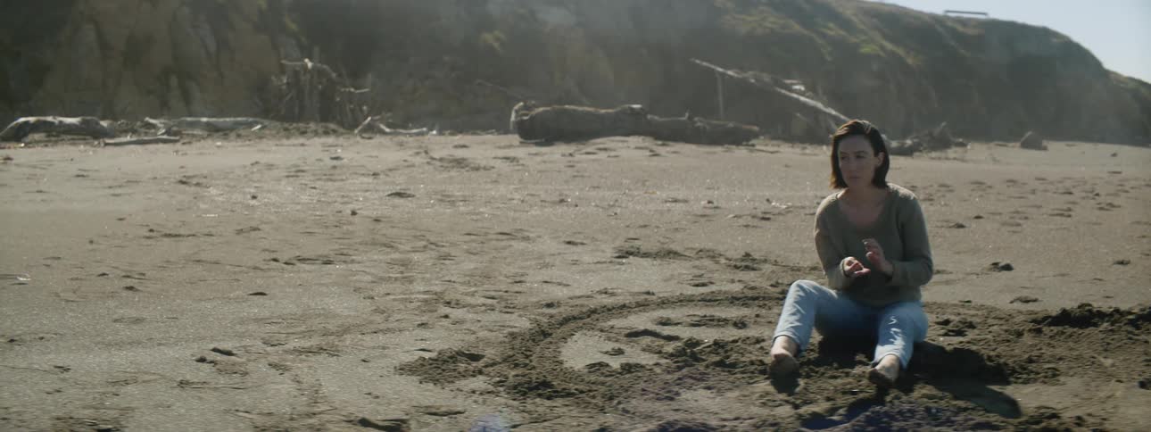 A woman sits in the sand on the edge of a drawn circle
