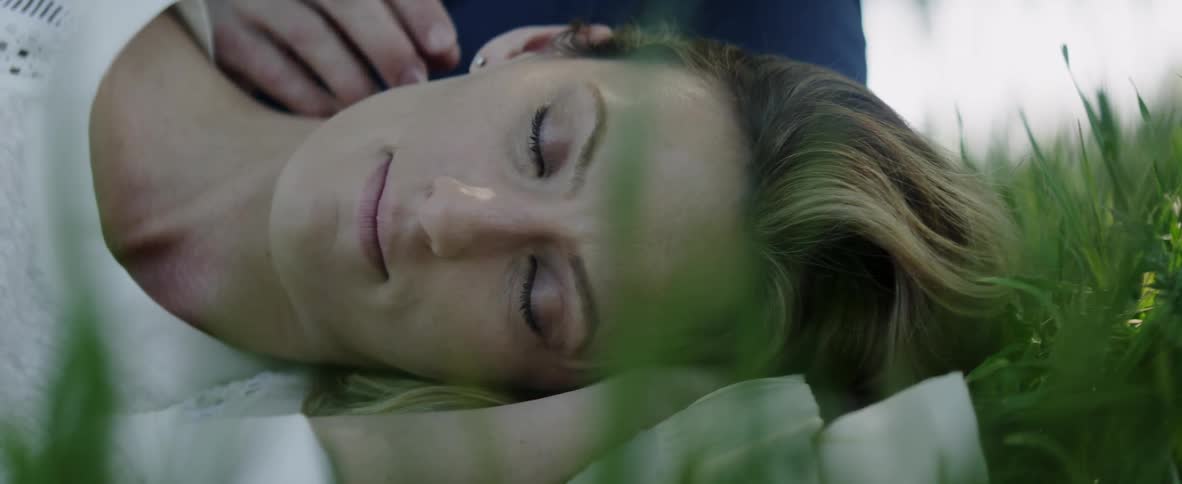 A man is stroking the hair and neck of a woman lying on the ground outside in daylight