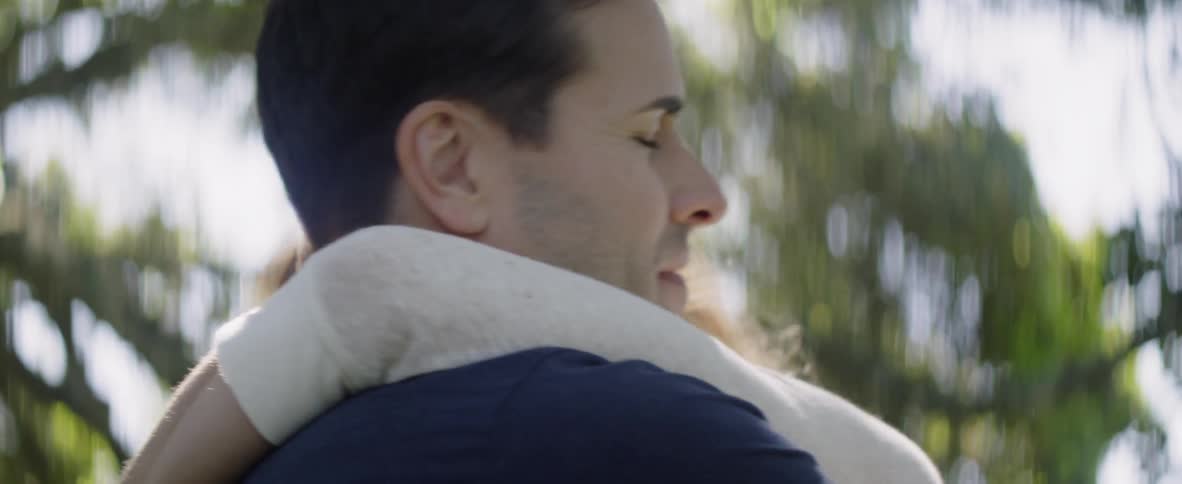 A man and woman hug under a tree in the sunshine
