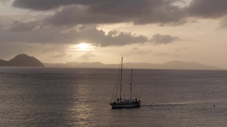 Boat sailing on open ocean waters as sun sets on cloudy evening