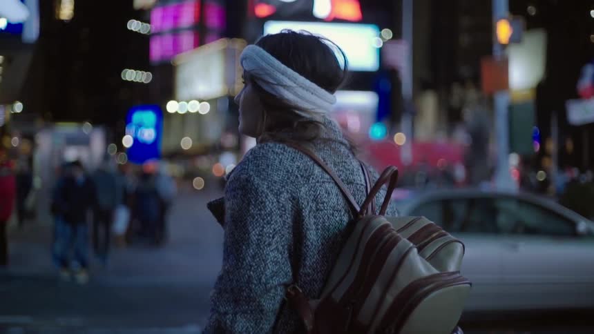 Woman wearing a backpack walking in a busy city at night