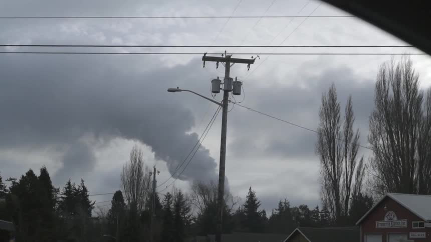 Driving through a town and passing a distant plume of smoke reaching up to the clouds