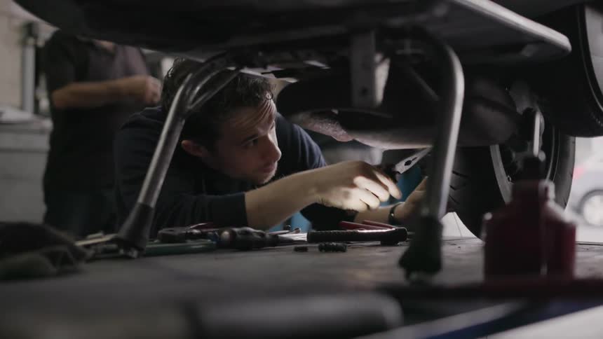 The man is shining a flashlight as he fixes something