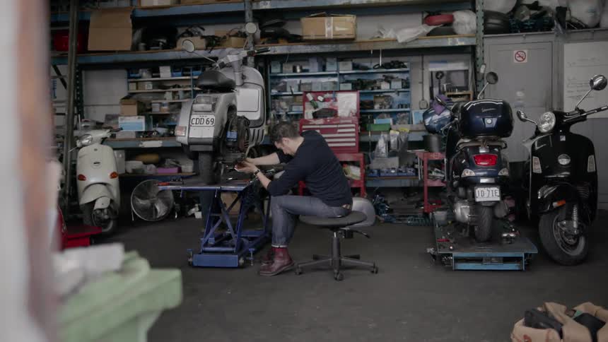 Two men are working inside a moped repair garage during the day
