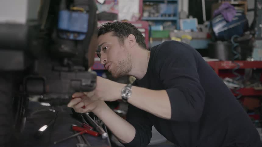 Man fixes on a small motorbike in a garage