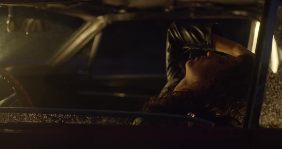A woman sitting in a car at night is leaning back and holding her head