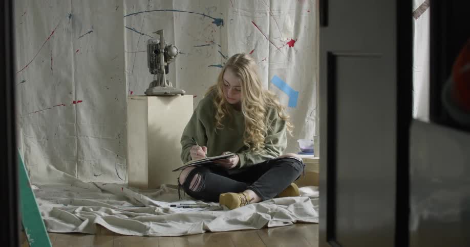 Artist Student is writing in a notebook sitting on a tarp