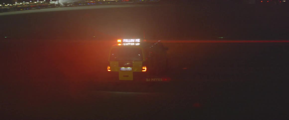 Yellow vehicle with lights flashing on top drives in a parking lot