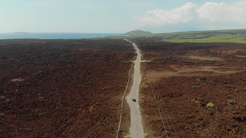 A car travels on an empty road that leads to the ocean