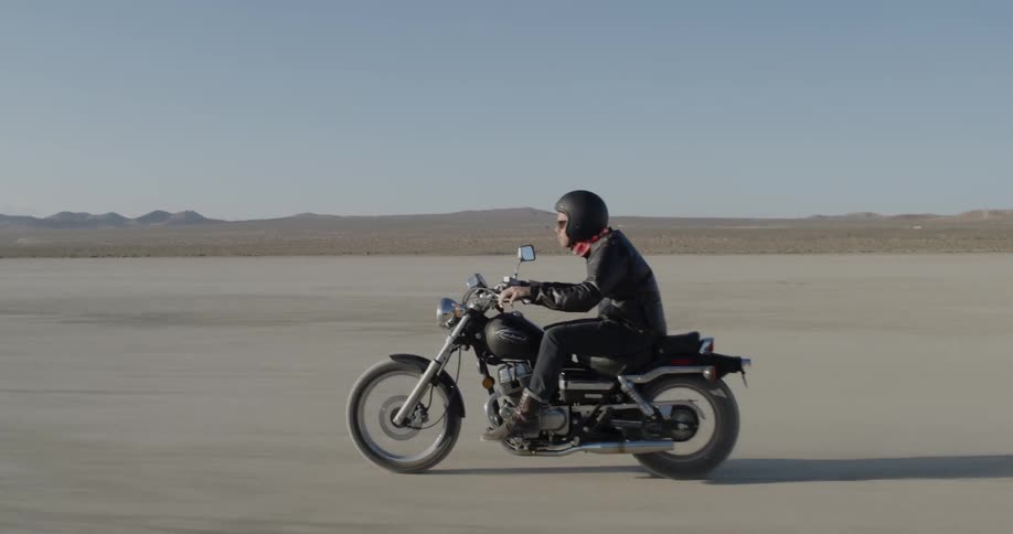 Man rides motorcycle through flat desert