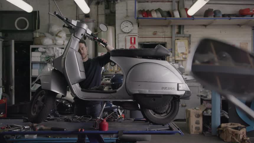 A man makes adjustment to the handlebar of a scooter on a workbench