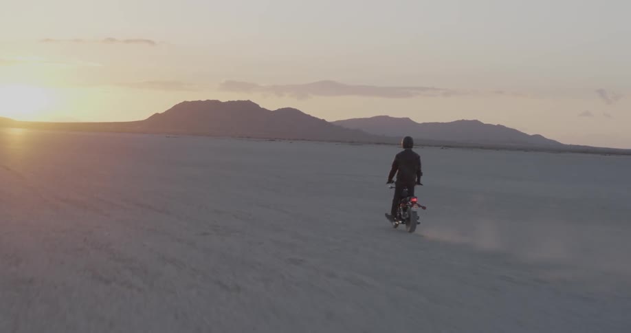 Person rides motorbike across flat desert at sunset