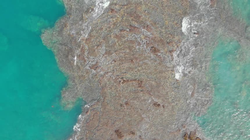 Water flows around a large rock in the ocean
