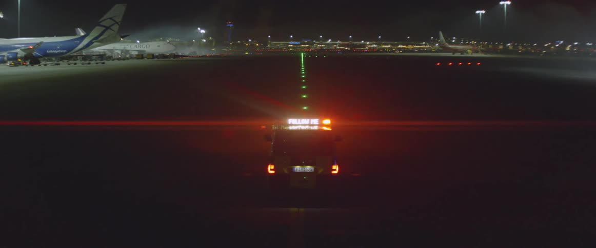 A vehicle with lights flashing is driving at an airport during the night