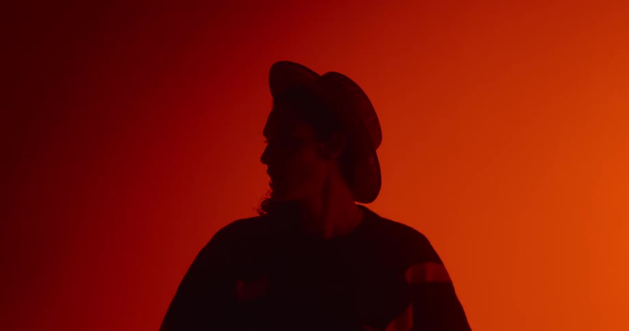 A man wearing a hat sings while colored lights flash
