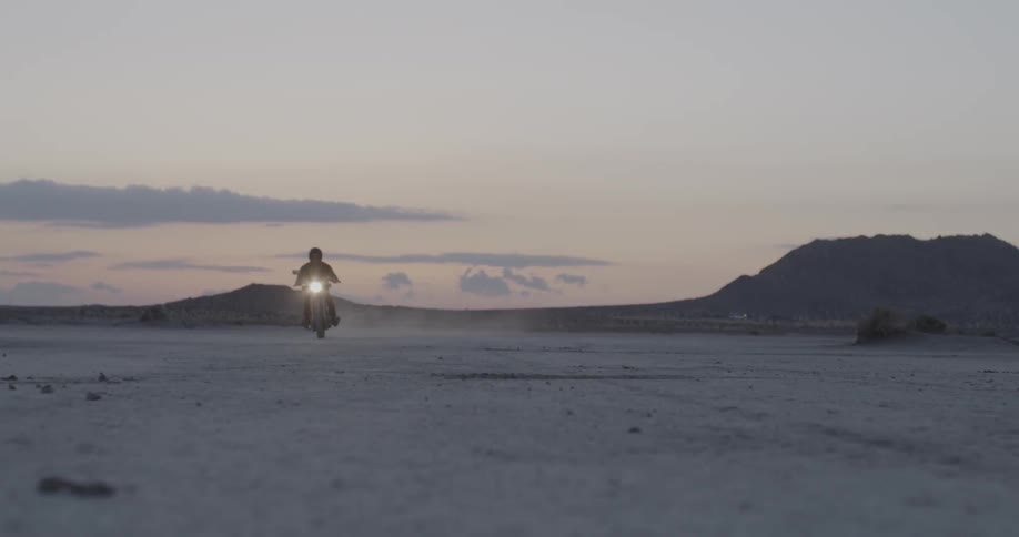 Person rides motorbike across flat desert at sunset
