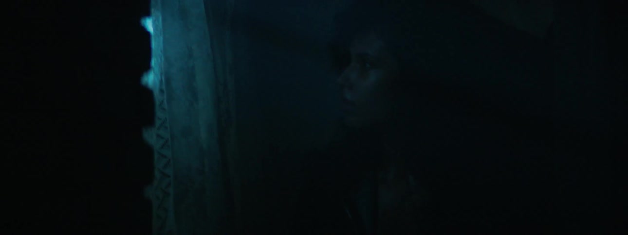 A woman stands next to a window in a dark room