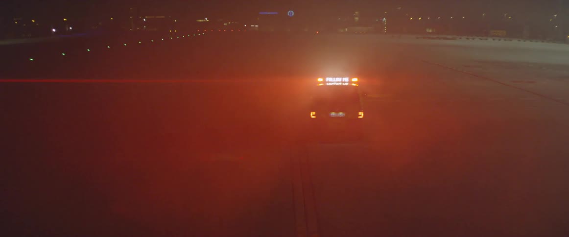 A vehicle with lights flashing travels on the tarmac at night
