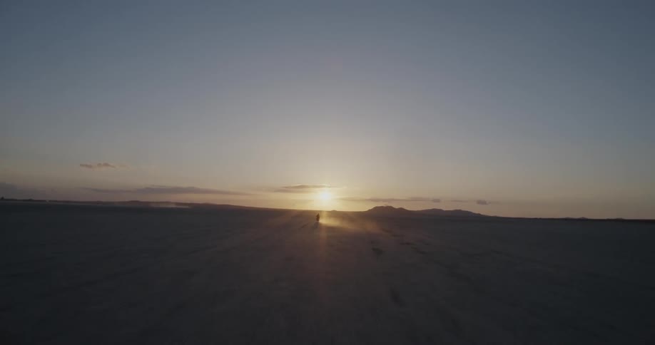 A motorcycle kicks up dust as it travels on the desert at sunset
