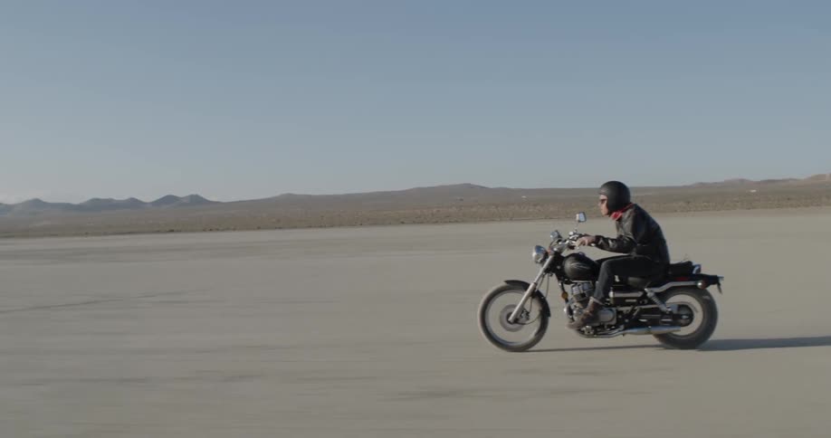 Person rides motorbike across flat desert at sunset