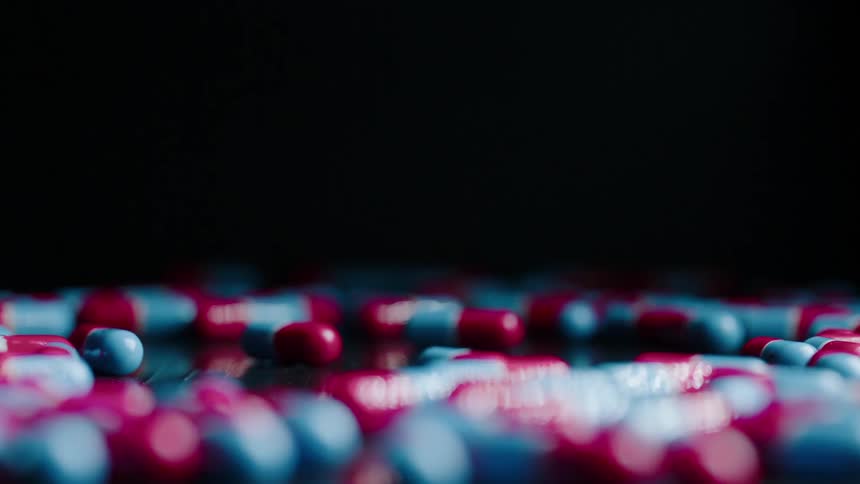Capsules of medicine are wobbling on a surface in daylight