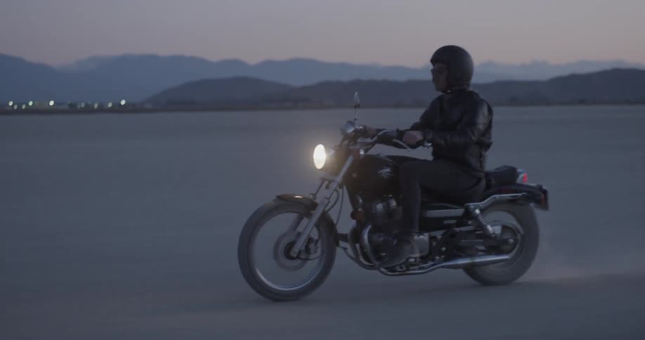 A man drives a motorcycle on a dirt plain at sunset