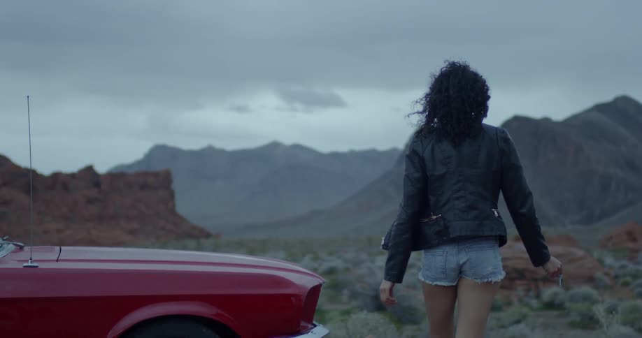 Woman walks past a red car in the country