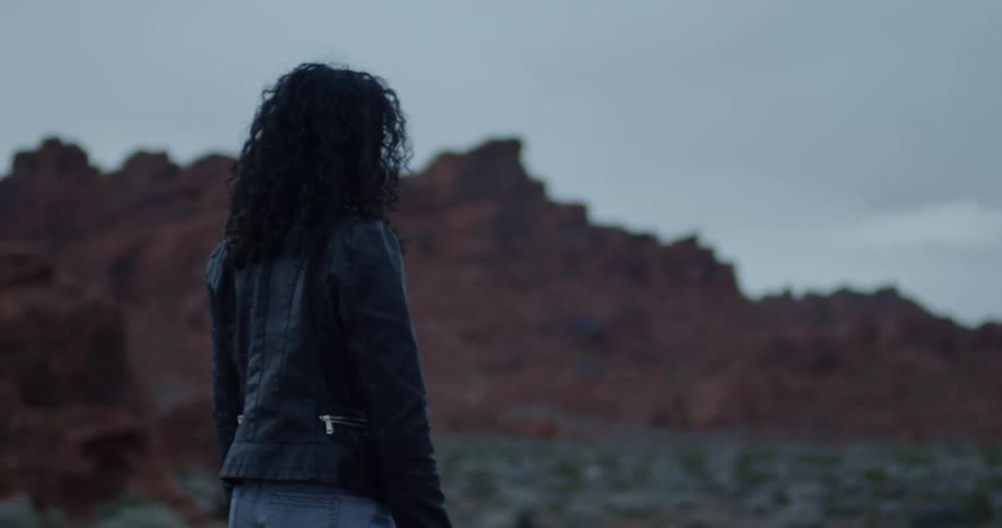 A woman is standing in the desert on a cloudy day
