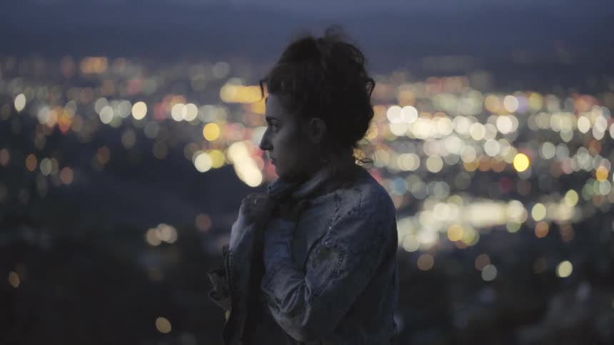 A woman stands above a cityscape at night