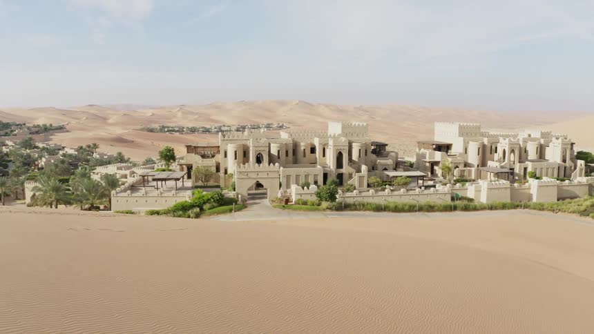 Many stone buildings sit on the sand under a blue sky
