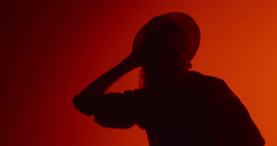 Woman holds her hat while she dances in a red lighted room