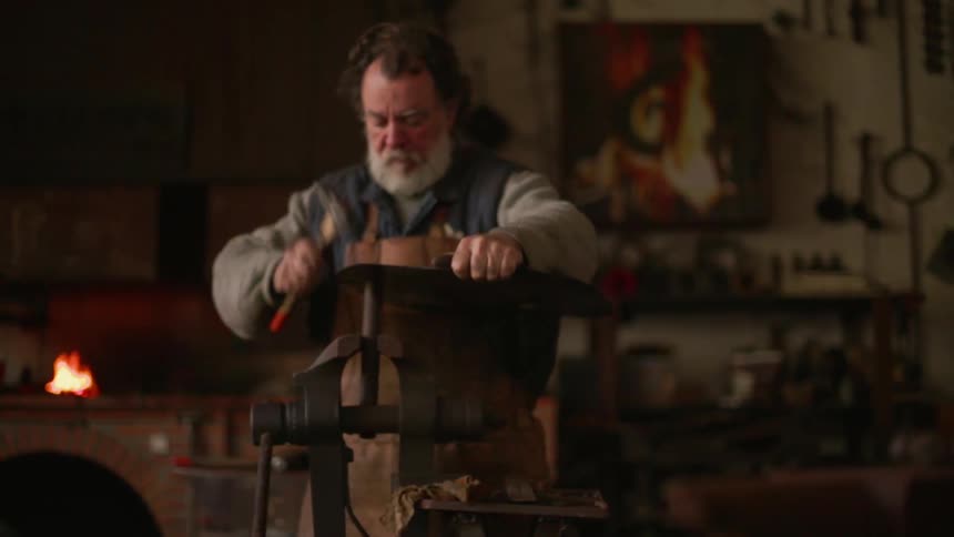 An artisan is hammering a metal plate in a workshop in daylight