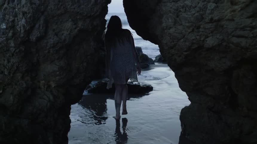 A woman walks under a rock formation on the beach