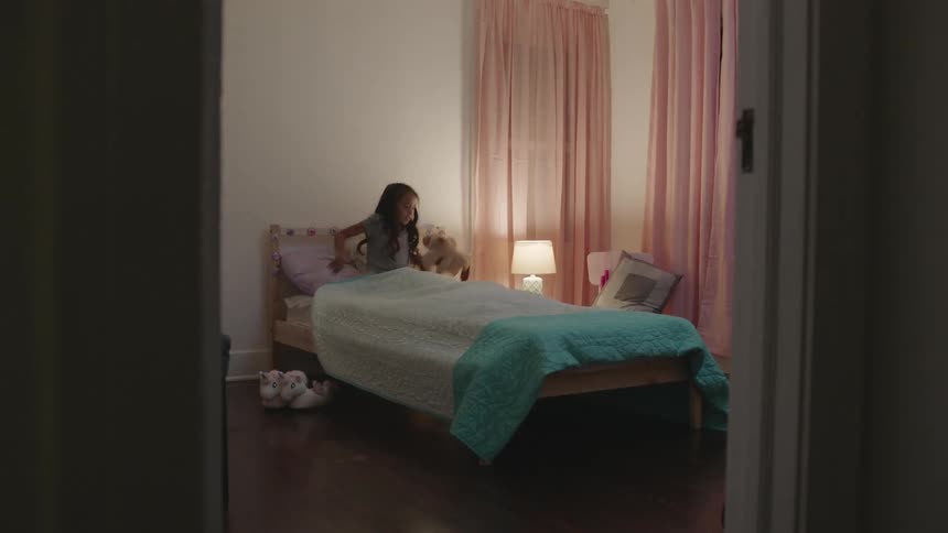 A girl climbs into bed with a stuffed animal