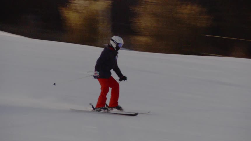 A young person is skiing down a training slope at dusk