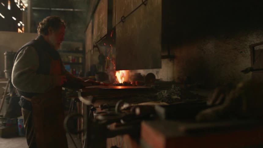 An artisan is stoking a forge in a workshop during the day