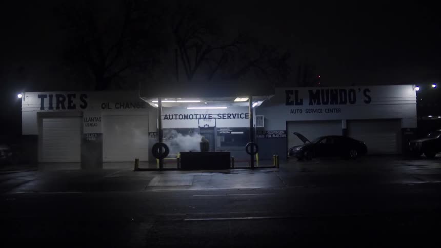 A white man stands outside an automotive services business at night