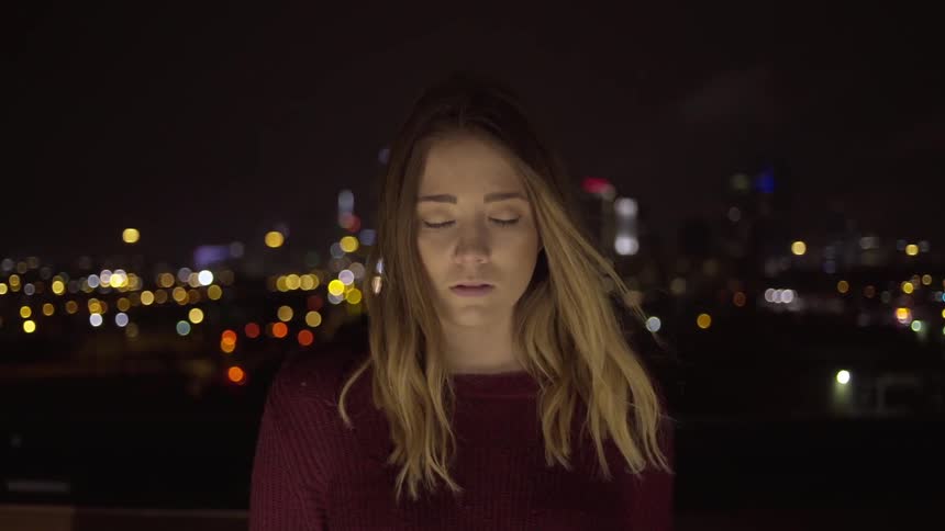 A woman stands in front of a night cityscape