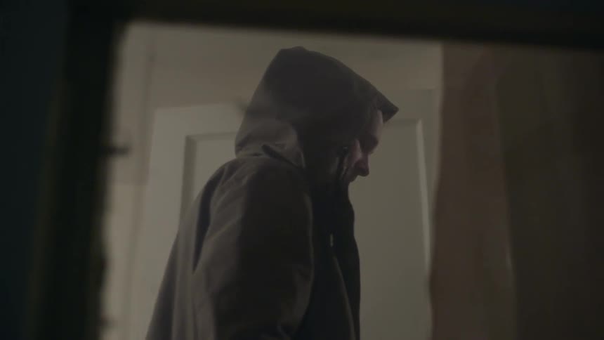 Close up of a hooded man walking through a room