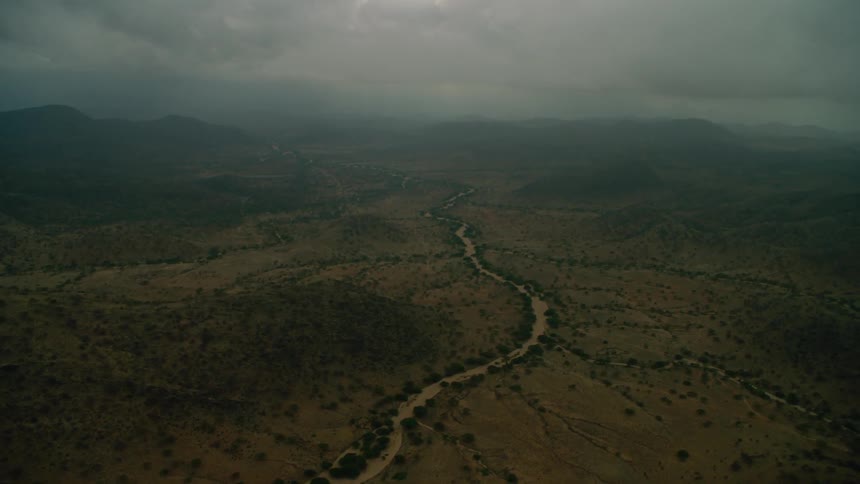 A muddy river bed winds through a barren landscape on a cloudy day
