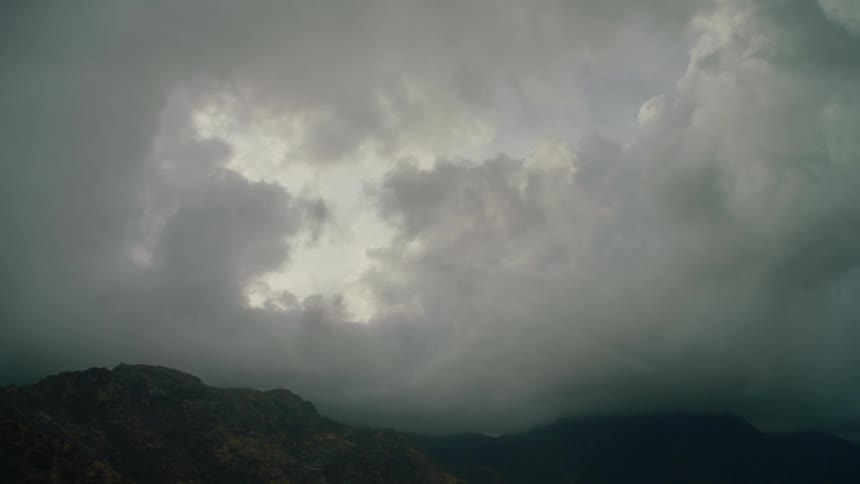 Clouds hover low and touch hill tops with the sun shining behind